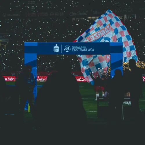 Na zdjęciu widać stadion sportowy, na którym odbywa się ceremonię powitania z flagami oraz migającymi światłami w tle.