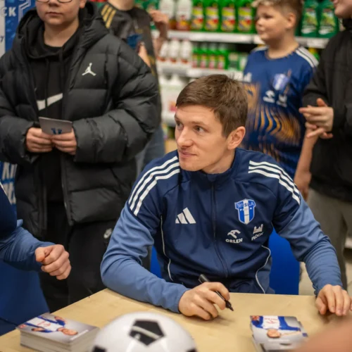 Na zdjęciu widoczni są zawodnicy, którzy podpisują autografy dla fanów w sklepie, otoczeni grupą młodych kibiców.