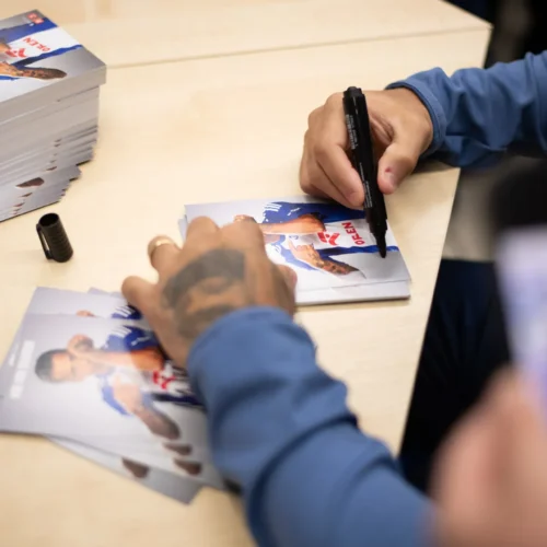 Na zdjęciu widać osobę podpisującą zdjęcia na tle stosu wyłożonych kart.