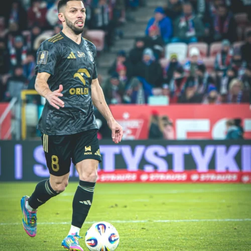 Na zdjęciu widoczny jest piłkarz w czarnej koszulce z numerem 8, który gra w piłkę na boisku podczas meczu.