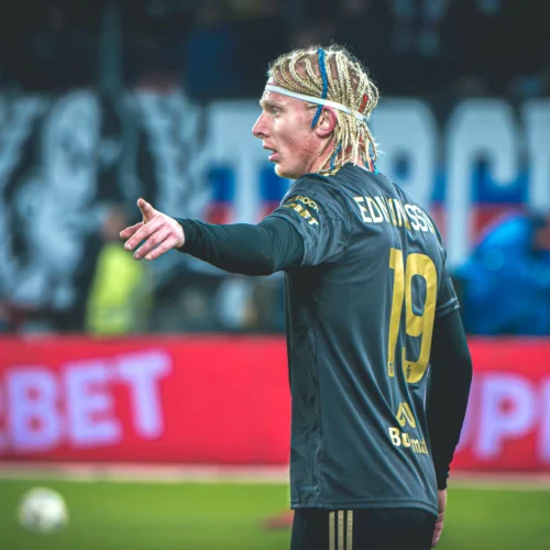 Na zdjęciu widoczny jest piłkarz podczas meczu, wskazujący gestem na boisku w czarnym uniformie z numerem 19.