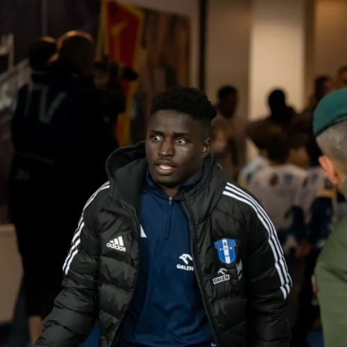 Na zdjęciu młody mężczyzna w czarnej kurtce sportowej z logiem klubu wygląda na zaniepokojonego, wchodząc do tunelu na stadionie.