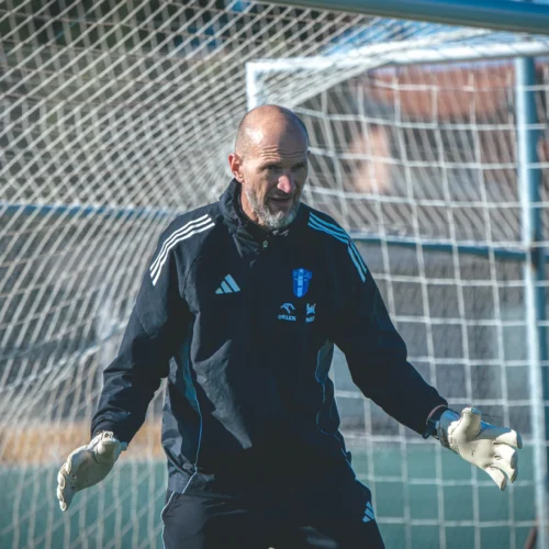 Na zdjęciu znajduje się bramkarz w rękawicach, który przygotowuje się do interwencji na boisku piłkarskim.