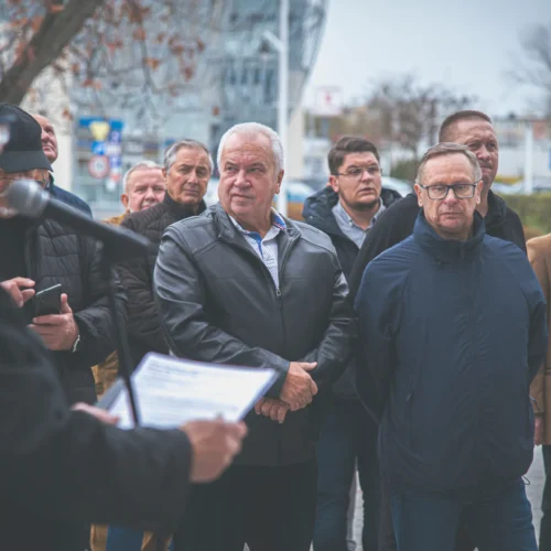 Grupa mężczyzn słuchająca przemówienia na zewnątrz w chłodny dzień.