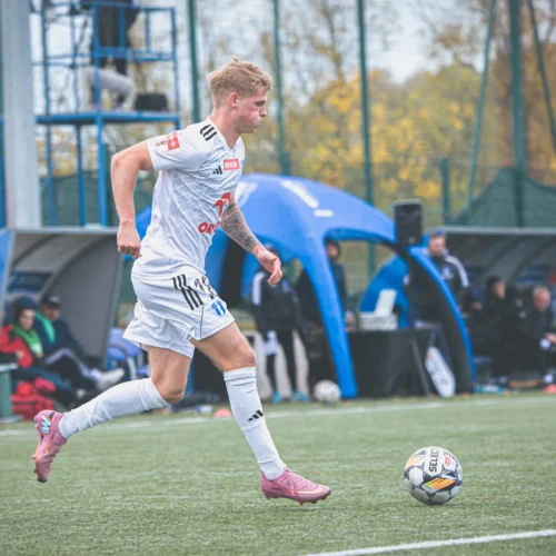 Na zdjęciu widoczny jest piłkarz biegnący w kierunku piłki na boisku sportowym.