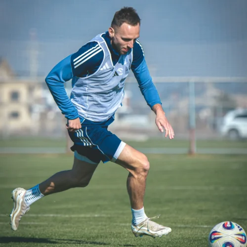 Mężczyzna w stroju piłkarskim biegnie po boisku, kierując się w stronę piłki.