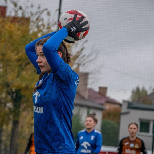 Na zdjęciu widać zawodniczkę w niebieskim stroju, przygotowującą się do wykonania rzutu z autu podczas meczu piłki nożnej.