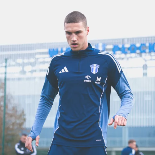 Na zdjęciu widać młodego mężczyznę w niebieskim stroju sportowym, który intensywnie ćwiczy na boisku piłkarskim.