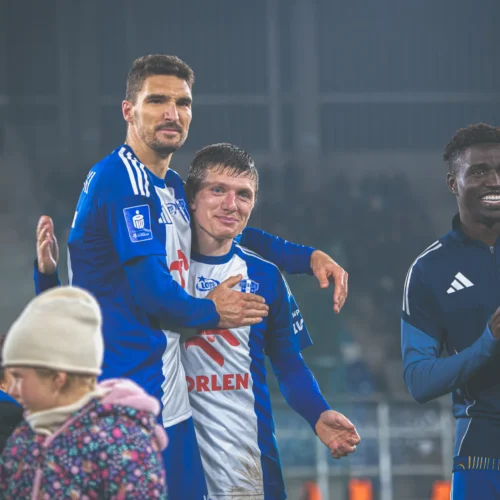 Na zdjęciu widać radosnych piłkarzy, którzy celebrują sukces po meczu, przytulając się i uśmiechając do kamery.