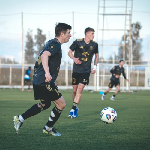 Na zdjęciu przedstawiono grupę piłkarzy biegających po zielonym boisku, koncentrujących się na piłce.