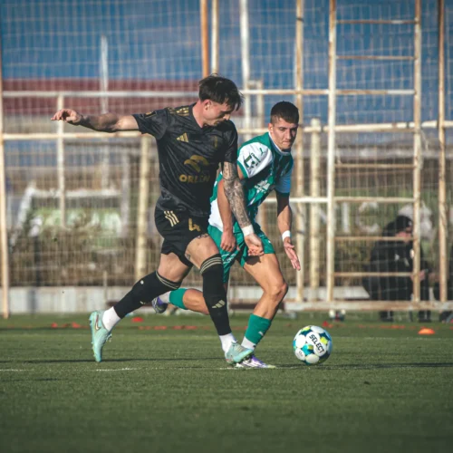 Dwoje piłkarzy rywalizuje o piłkę na boisku, podczas treningu lub meczu.