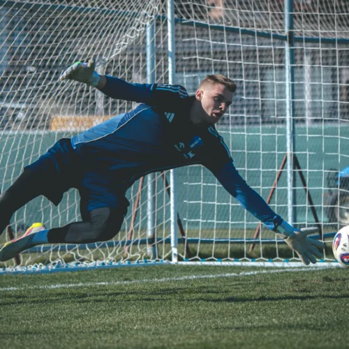 Bramkarz skacze do piłki podczas treningu na boisku piłkarskim.