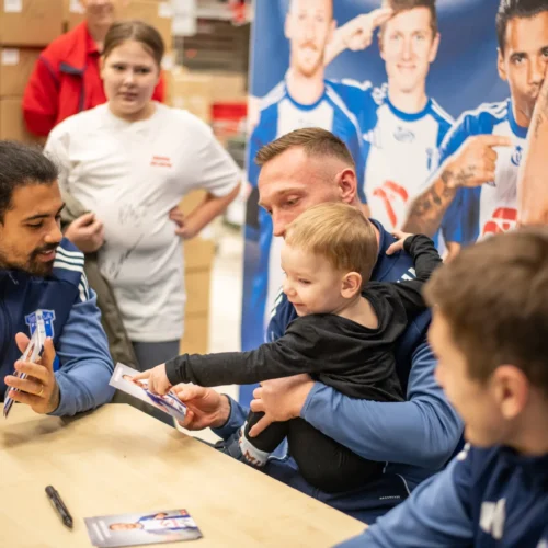 Na zdjęciu widać piłkarzy podpisujących autografy dla dzieci podczas wydarzenia promocyjnego.