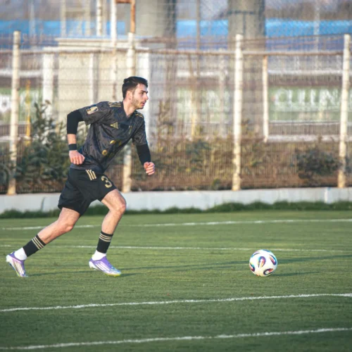 Na zdjęciu widać piłkarza w ruchu, który biegnie po boisku podczas treningu, w tle znajduje się bramka i flagi rogu.