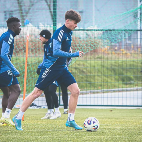 Na zdjęciu trzech zawodników piłkarskich uczestniczy w treningu na boisku, z piłką widoczną na pierwszym planie.