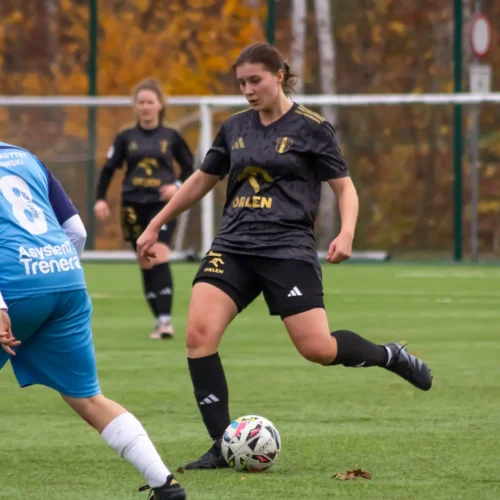 Na zdjęciu widoczne są zawodniczki grające w piłkę nożną na boisku, w otoczeniu jesiennych kolorów.