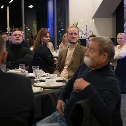 Zdjęcie przedstawia grupę ludzi siedzących przy elegancko nakrytym stole w nowoczesnej restauracji, wśród jasnych świec i stylowych dekoracji.