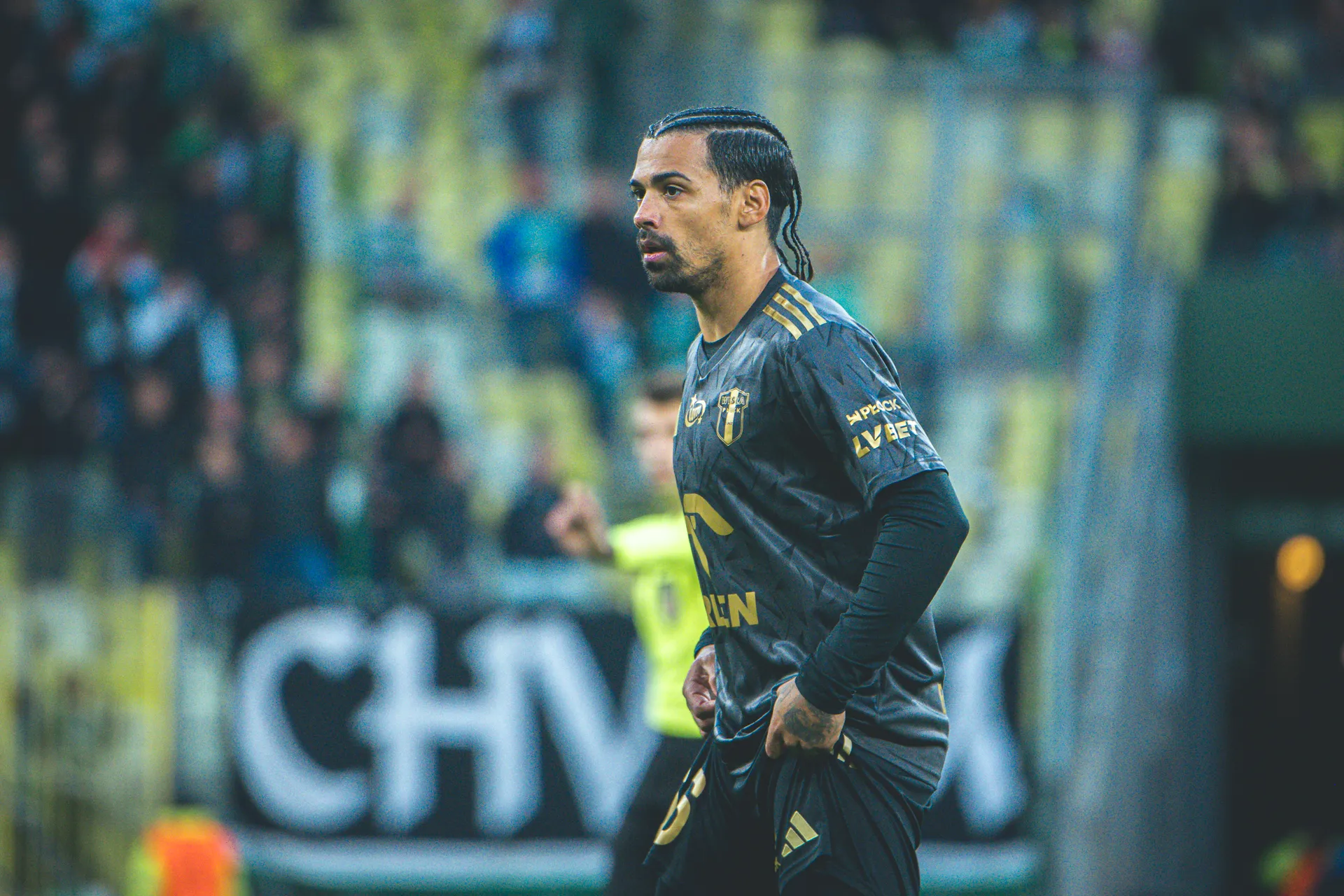 Na zdjęciu widoczny jest zawodnik piłkarski w ciemnoszarym stroju, stojący na boisku z widocznie skupionym wyrazem twarzy.