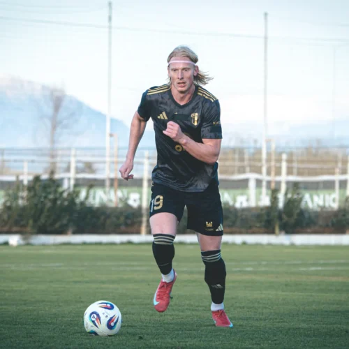 Na zdjęciu widać zawodnika w czarnej koszulce biegającego z piłką na boisku.