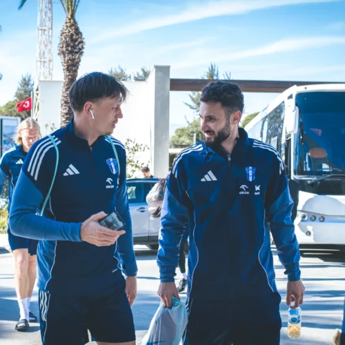 Grupa sportowców w uniformach idzie w kierunku autobusu, rozmawiając i przygotowując się do podróży.