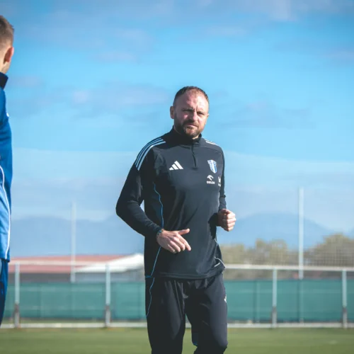 Na zdjęciu widoczny jest mężczyzna w sportowej odzieży, który biega na boisku piłkarskim pod jasnym niebieskim niebem.
