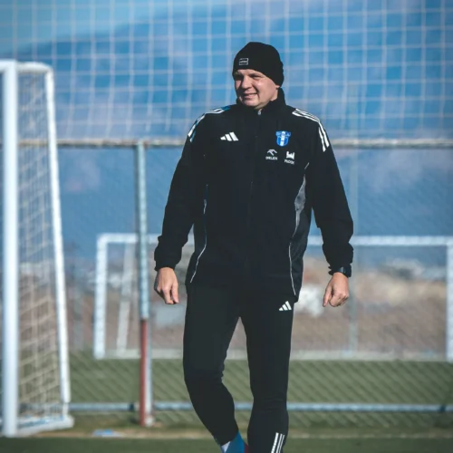 Na zdjęciu widać zawodnika w czarnej odzieży sportowej, który stoi na boisku piłkarskim, trzymając piłkę przy nodze.