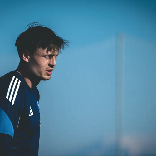 Na zdjęciu widoczny jest mężczyzna w sportowym ubraniu, patrzący w dal na tle nieba.