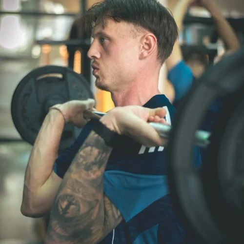 Mężczyzna trenujący na siłowni, wykonujący przysiad ze sztangą na plecach.