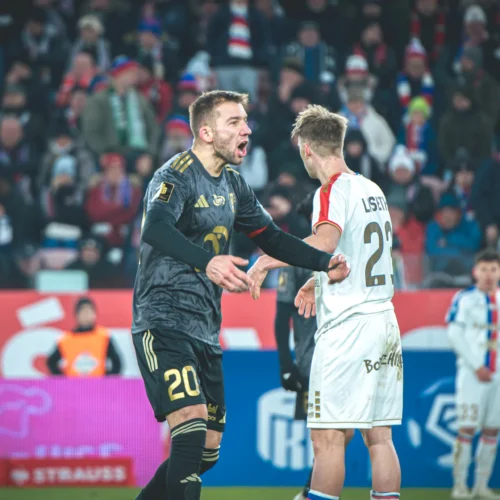 Zawodnicy piłkarscy dyskutują podczas meczu na tle kibiców na trybunach.