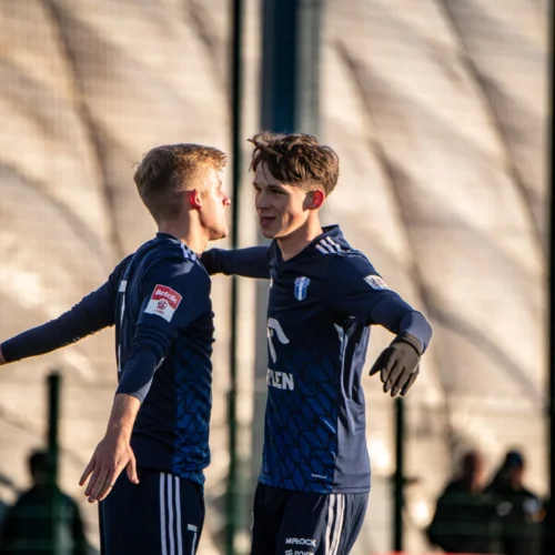 Na zdjęciu dwóch piłkarzy w niebieskich koszulkach celebruje udany moment na boisku.