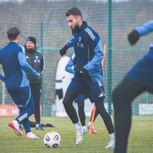 Zawodnicy trenują na boisku piłkarskim w zimowej scenerii.