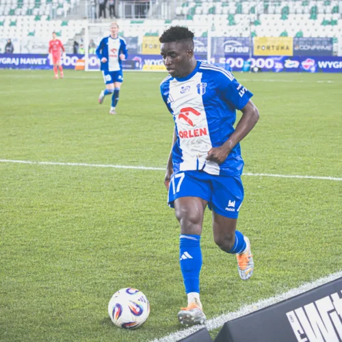 Zawodnik w niebiesko-białym stroju piłkarskim przygotowuje się do wykonania rzutu rożnego na boisku w trakcie meczu.