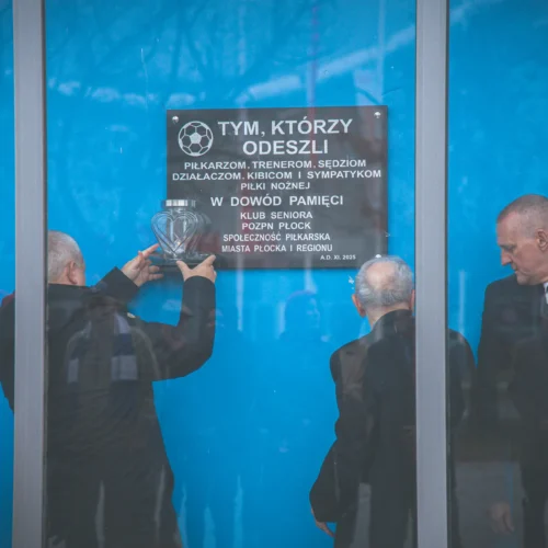 Na zdjęciu przedstawiono ceremonie odsłonięcia tablicy pamiątkowej w hołdzie piłkarzom, trenerom oraz działaczom sportowym, z udziałem mężczyzn w garniturach.