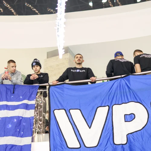 Na zdjęciu widać grupę młodych ludzi stojących na balkonie i trzymających dużą niebieską flagę z wyraźnym napisem "IVPU".