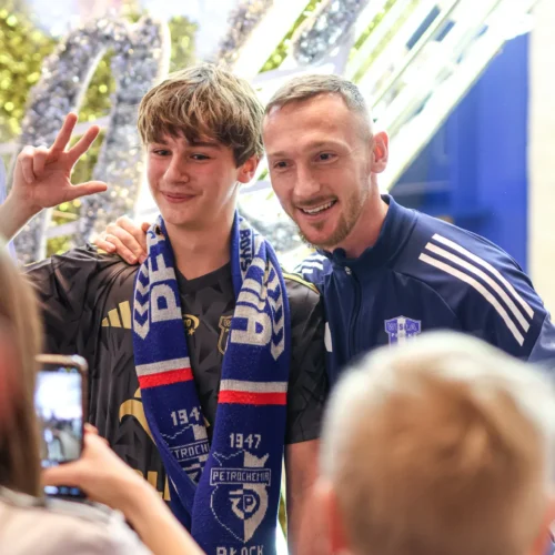 Na zdjęciu dwóch młodych mężczyzn robi zdjęcie z kibicem, który ma na sobie szalik drużyny Wisła Płock, w tle widoczne dekoracje.