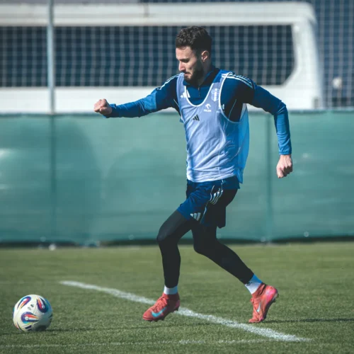 Na zdjęciu widoczny jest mężczyzna w niebieskim stroju sportowym, który biega po boisku piłkarskim, przygotowując się do treningu.