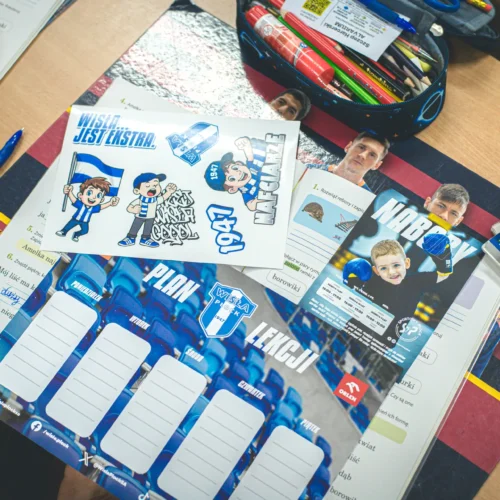 Na zdjęciu widać biurko dziecka z zeszytem, materiałami do nauki oraz kolorowymi rysunkami i gadżetami związanymi z drużyną sportową.