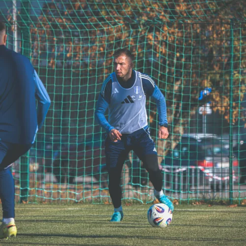 Na zdjęciu widać kilku piłkarzy trenujących na boisku, koncentrujących się na grze z piłką w pobliżu siatki.