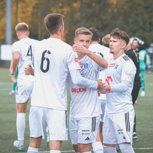 Na zdjęciu widoczni są piłkarze w białych strojach, którzy celebrują wspólny sukces na boisku.