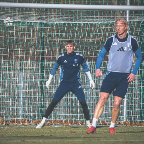 Na zdjęciu widać bramkarza w akcji podczas treningu piłkarskiego oraz zawodnika na boisku.