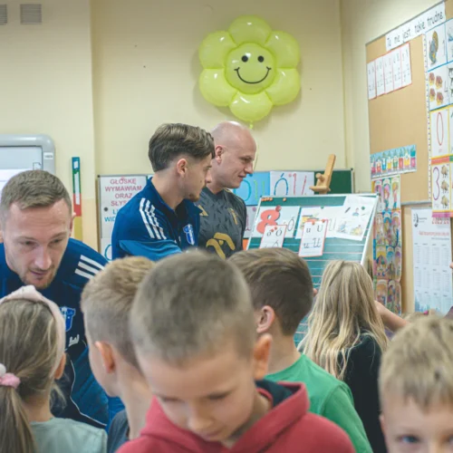 Na zdjęciu w klasie widać nauczycieli oraz uczniów, którzy wspólnie uczestniczą w zajęciach edukacyjnych.