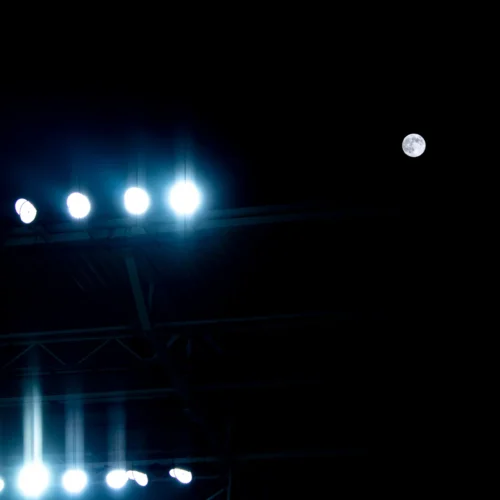 Na zdjęciu widać oświetlenie stadionu na tle nocnego nieba z widoczną pełnią księżyca.