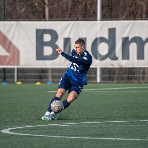 Na zdjęciu widać piłkarza w niebieskim stroju, który wykonuje kopnięcie piłki na boisku futbolowym.