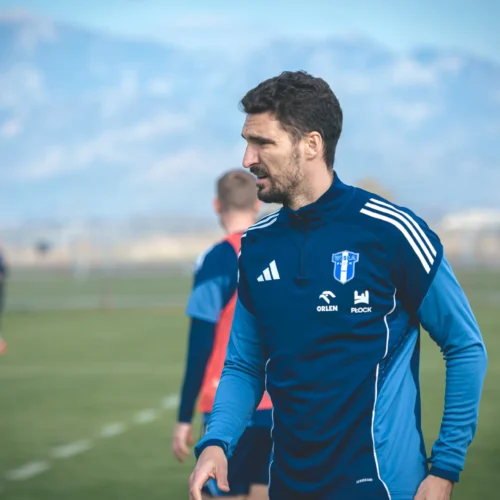 Na zdjęciu widać mężczyznę w niebieskiej odzieży sportowej podczas treningu piłkarskiego na tle gór.