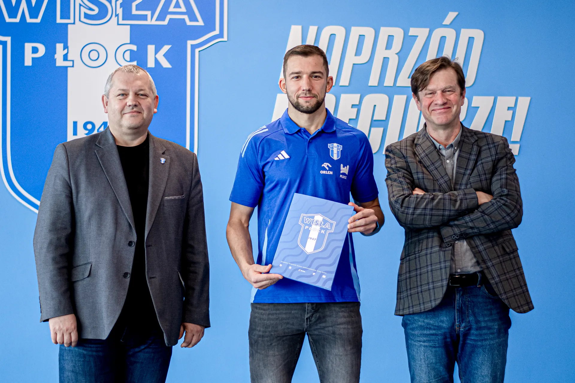 Na zdjęciu trzej mężczyźni stoją obok siebie, trzymający dokumenty związane z klubem Wisła Płock, na tle niebieskiej ściany z logo klubu.