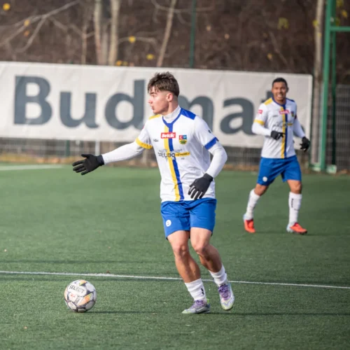 Młodzi piłkarze trenują na boisku, podczas meczu, w różnych kolorach strojów sportowych.
