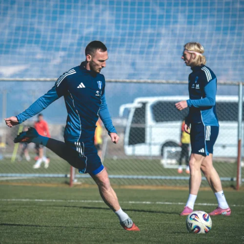 Dwaj piłkarze trenują na boisku, jeden z nich wykonuje ćwiczenie z piłką.