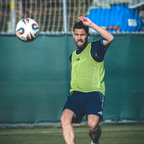 Na zdjęciu widać piłkarza w treningowym stroju, który jest w trakcie wykonywania podania piłki na boisku.