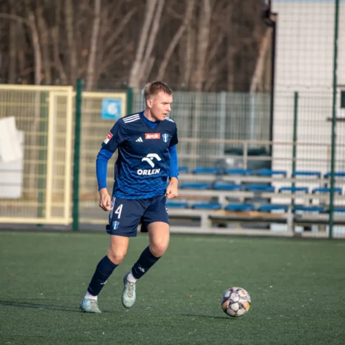 Na zdjęciu widoczny jest piłkarz w niebieskim stroju, który biegnie za piłką na boisku.