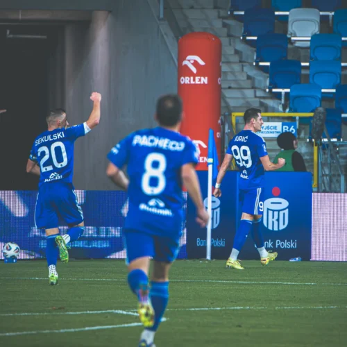 Na zdjęciu widoczni są piłkarze w niebieskich strojach celebrujący zdobycie bramki podczas meczu.